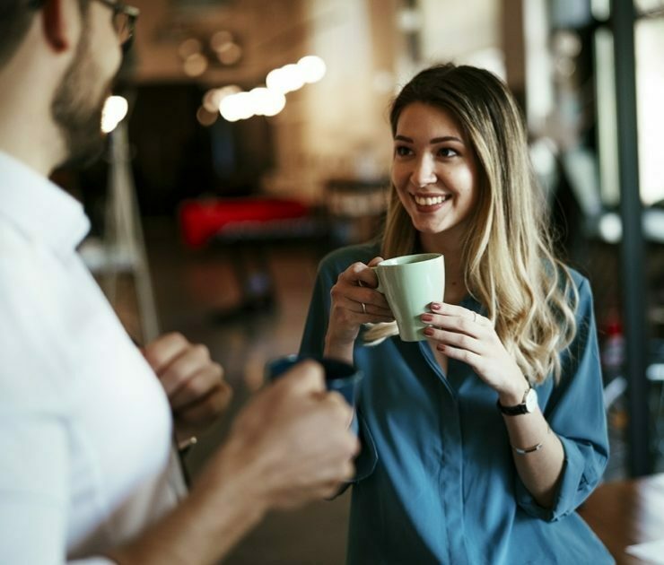 Female employee drinking coffee while speaking with co-worker